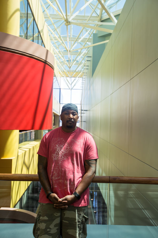 Male student standing in front of a railing overlooking a large room